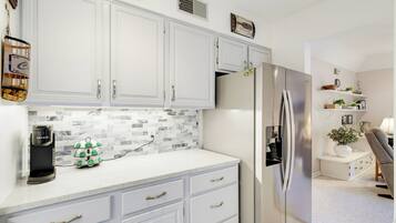 A modern kitchen with white cabinetry, a stainless steel refrigerator, and a coffee machine.
