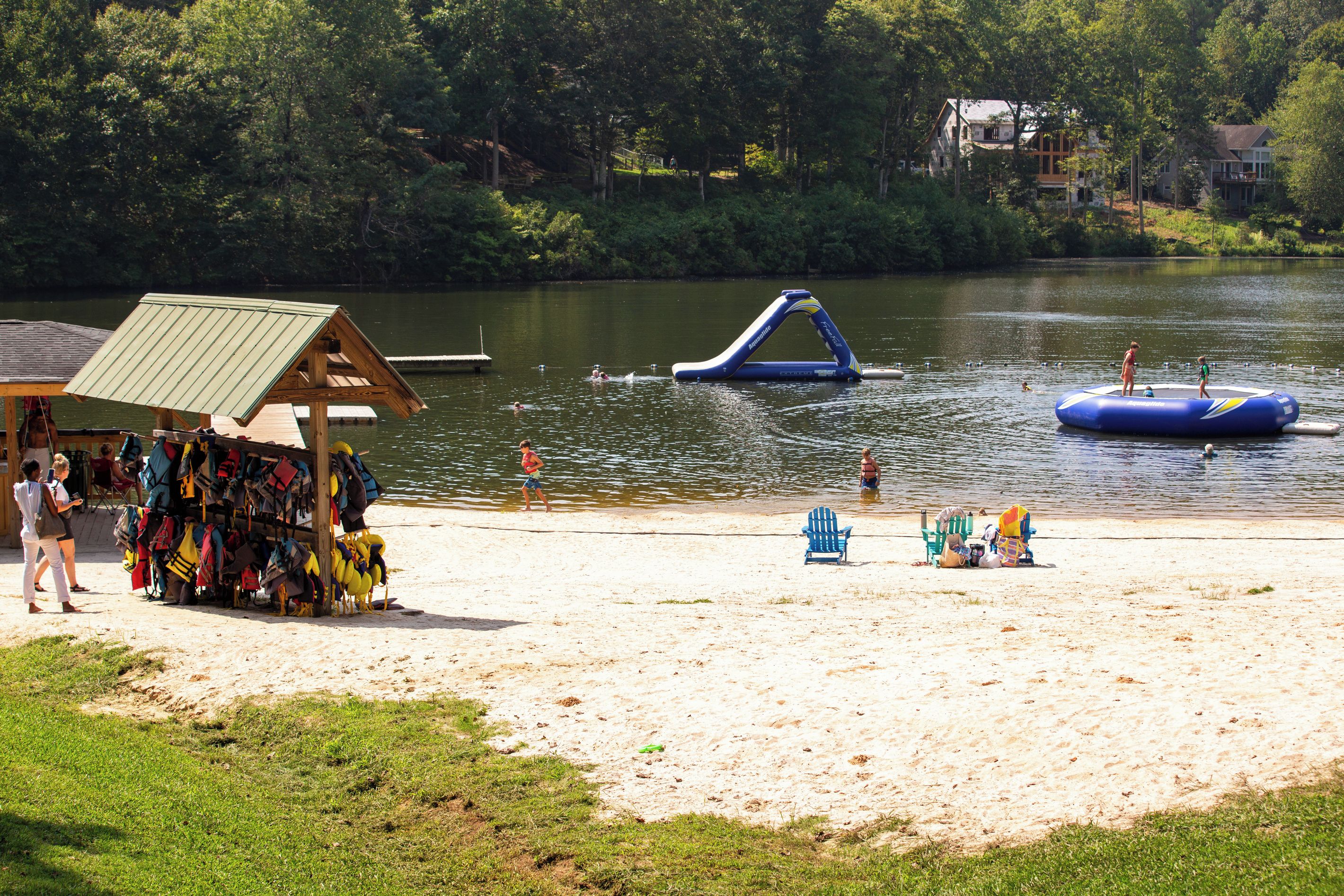 Une plage au bord d’un lac, avec un toboggan aquatique flottant, des chaises de plage et un petit bâtiment doté d’un toit végétalisé.