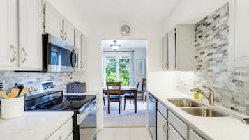 A modern kitchen with white cabinetry, stainless steel appliances, and a view to a dining area.