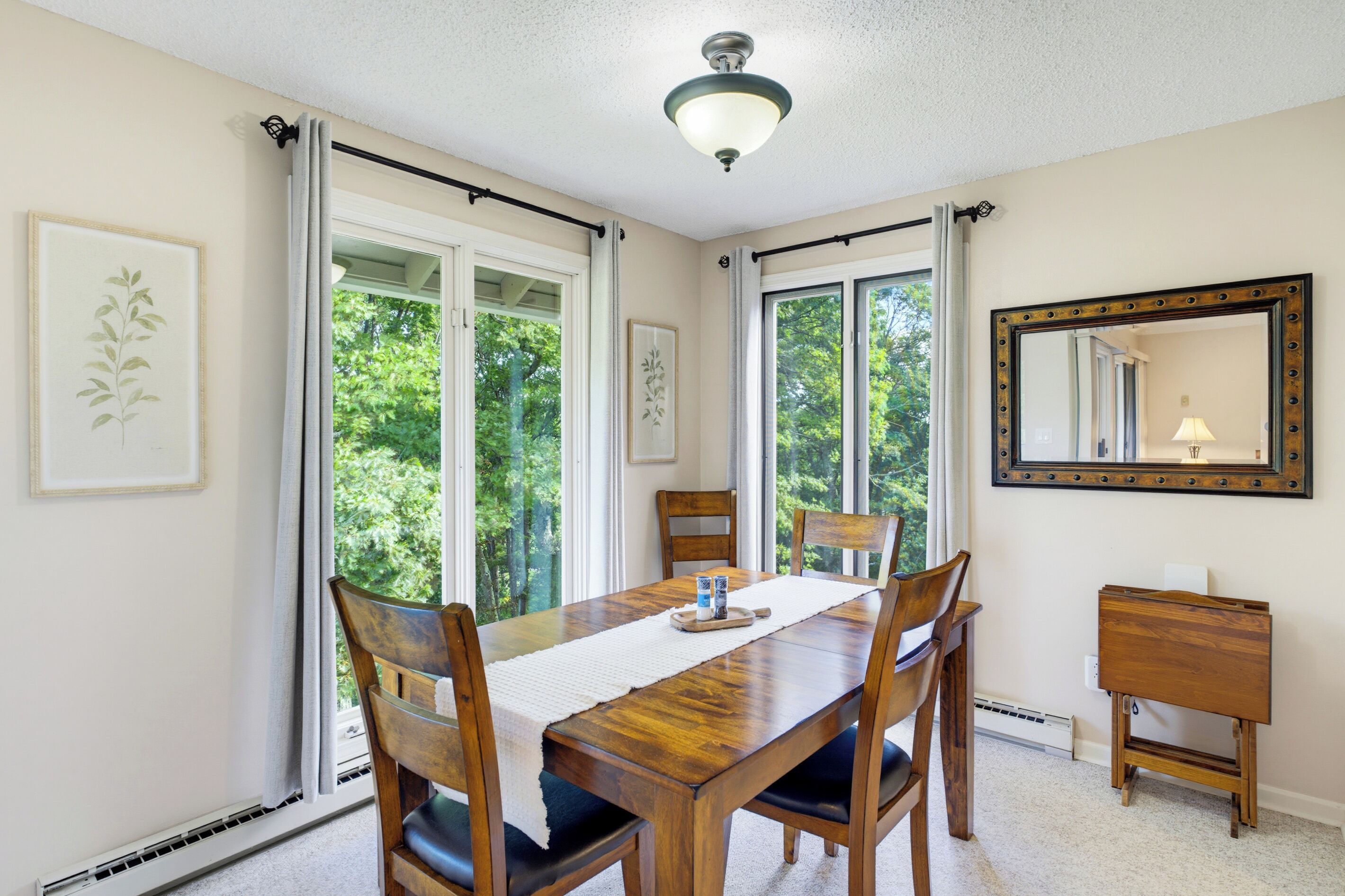 A dining room with a wooden table, chairs, a mirror, and framed artwork on the walls.