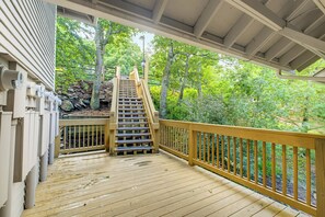 A wooden deck with a staircase leading to a covered area, surrounded by trees and greenery. - The Haven at Wintergreen Resort | Luxury 2BR Condo, 2 Kings & Golf View (Wintergreen Resort)