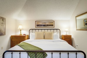 A neatly made bed with a headboard, two bedside tables with lamps, a framed picture above the bed, and a carpeted floor. - The Haven at Wintergreen Resort | Luxury 2BR Condo, 2 Kings & Golf View (Wintergreen Resort)