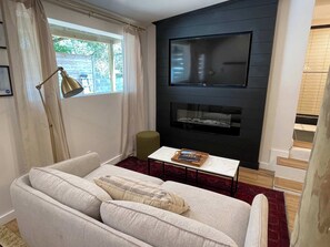 Ein Wohnzimmer mit einer Couch, einem Couchtisch, einem an einer schwarzen Wand befestigten Fernseher und einem Fenster mit Vorhängen.