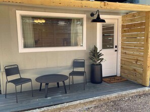 Eine Holzterrasse mit einem kleinen Tisch, zwei Stühlen, einem Blumentopf und einer Tür mit Fenster darüber.