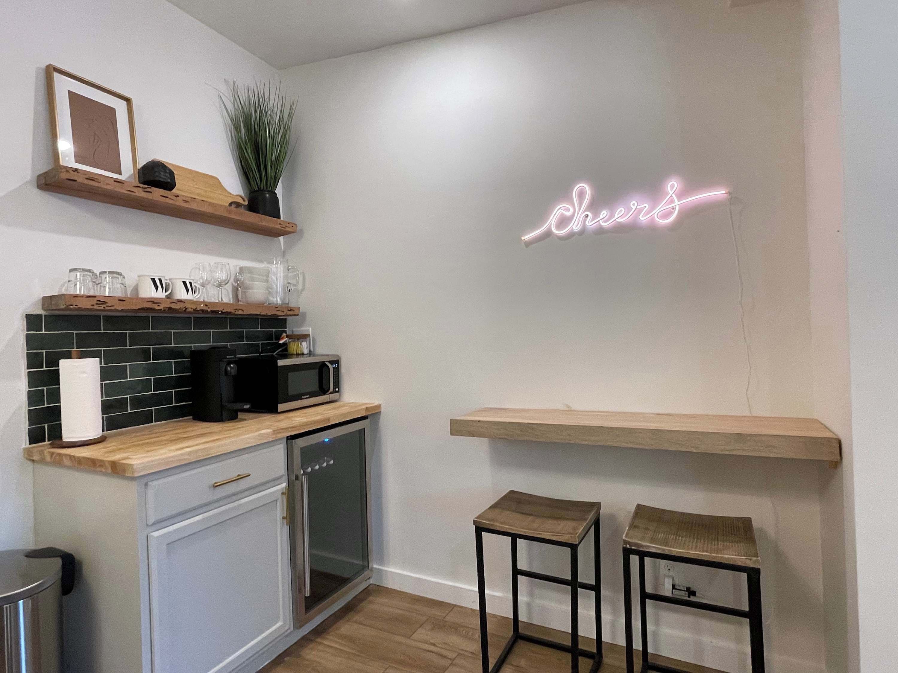 A modern kitchen with a neon sign, wooden shelves, and a microwave.