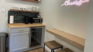 Una cocina con microondas, tostadora y horno de puerta de vidrio. Hay un letrero de neón en la pared y una estantería con cristalería.