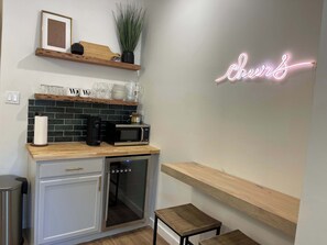 Eine Küche mit Mikrowelle, Toaster und Backofen mit Glastür. An der Wand befindet sich ein Neon-Schild und eine Ablage mit Gläsern.
