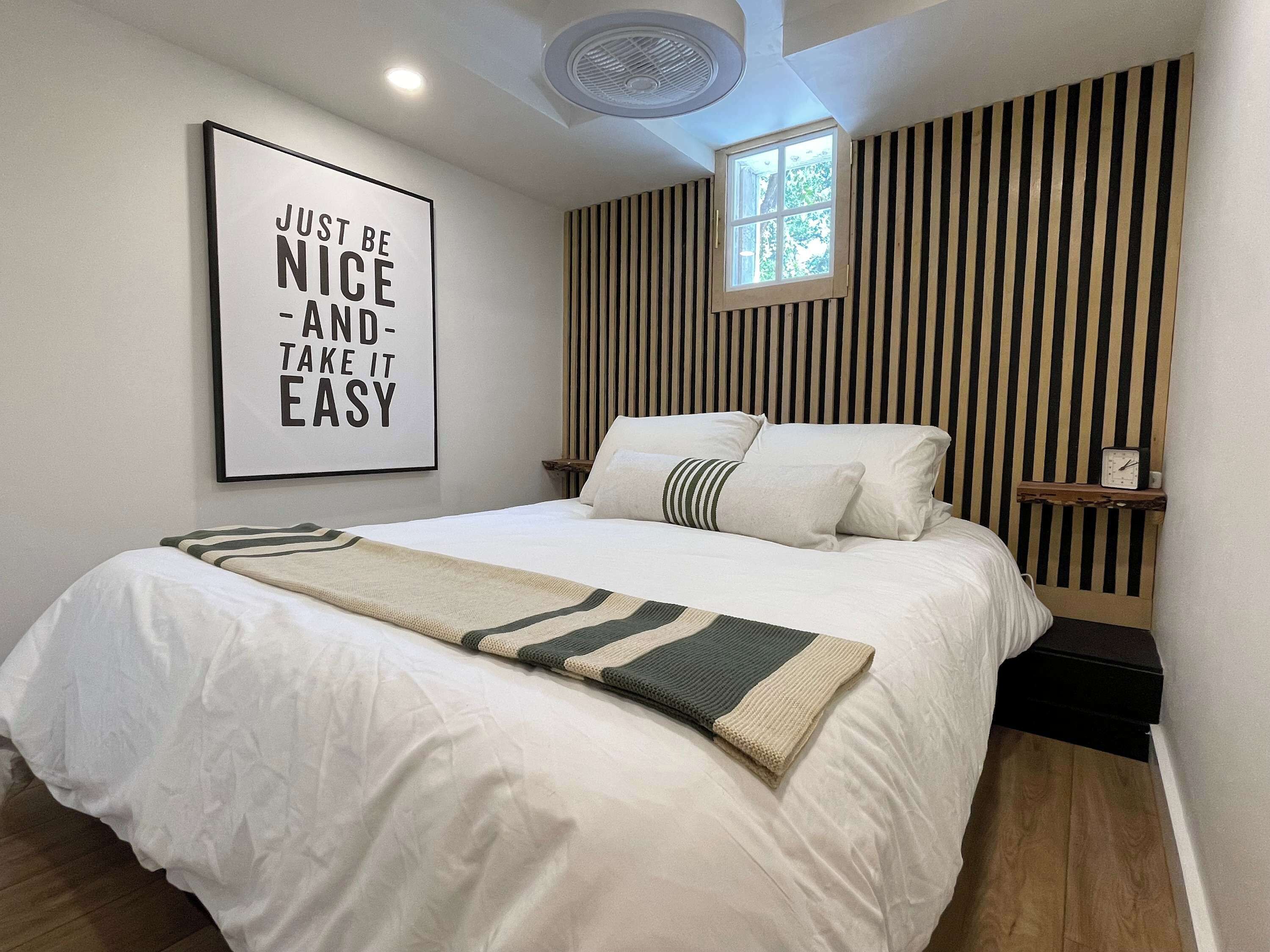 A neatly made bed with a striped throw, a wall-mounted clock, and a motivational poster.
