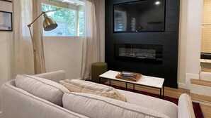 Una sala de estar moderna con sofá, mesa de centro, lámpara de pie, televisor de pantalla plana montado en una pared oscura y chimenea.