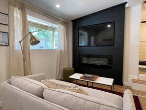 Ein modernes Wohnzimmer mit einer Couch, einem Couchtisch, einer Stehlampe, einem Flachbildfernseher an einer dunklen Wand und einem Kamin.
