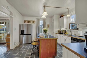 Een moderne keuken met een roestvrijstalen koelkast, een houten kookeiland met stoelen, en een bord waarop 'KITCHEN' staat.