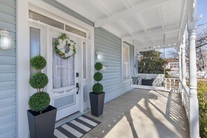 A porch with a covered seating area, a door with a wreath, and potted plants. - Pecan Grove Retreat - Pool & Fire pit (Fredericksburg)