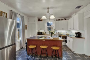 A kitchen with a central island, bar stools, a refrigerator, and cabinets. - Pecan Grove Retreat - Pool & Fire pit (Fredericksburg)
