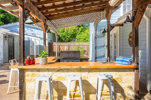 Een buitengebied met een bar, een grill, krukken en een houten pergola.