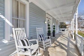 Eine Veranda mit zwei Schaukelstühlen, einem Blumentopf und einem weißen Zaun.