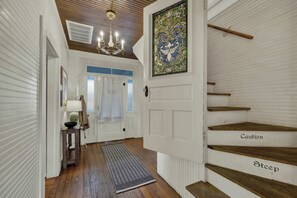 A hallway with a wooden floor, a chandelier, a stained glass window, and a staircase with 'Caution' and 'Steep' signs. - Pecan Grove Retreat - Pool & Fire pit (Fredericksburg)
