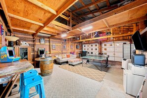 A rustic interior with wooden beams, a ping pong table, a sofa, and a bar area. - Pecan Grove Retreat - Pool & Fire pit (Fredericksburg)