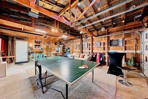 Ein Pingpong-Tisch in einem rustikalen Raum mit Holzbalken, einer Dartscheibe und verschiedenen Sportgeräten.