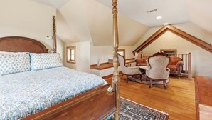 Ein Schlafzimmer mit Himmelbett, Holzboden und einer Sitzecke mit Sessel und Sofa.