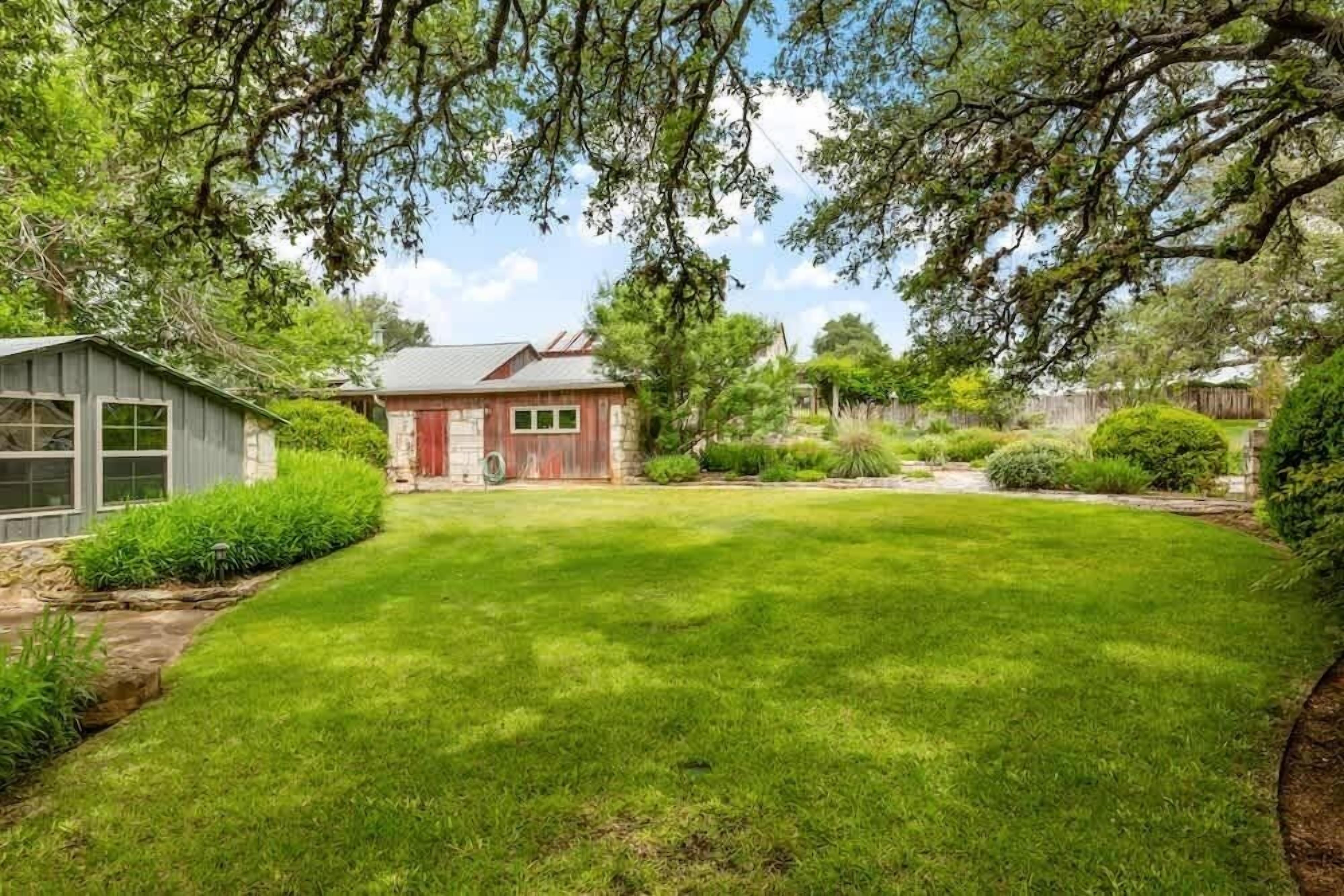 Een achtertuin met een verzorgd gazon, een houten tuinhuisje en een rode schuurachtige constructie.