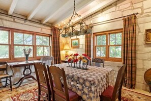 A dining room with a table set for four, a chandelier, and a view through large windows. - Fred Haus - Historic home with Hot Tub & Fire Pit (Fredericksburg)