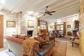 A spacious living room with a stone fireplace, comfortable seating, and a ceiling fan. - Fred Haus - Historic home with Hot Tub & Fire Pit (Fredericksburg)