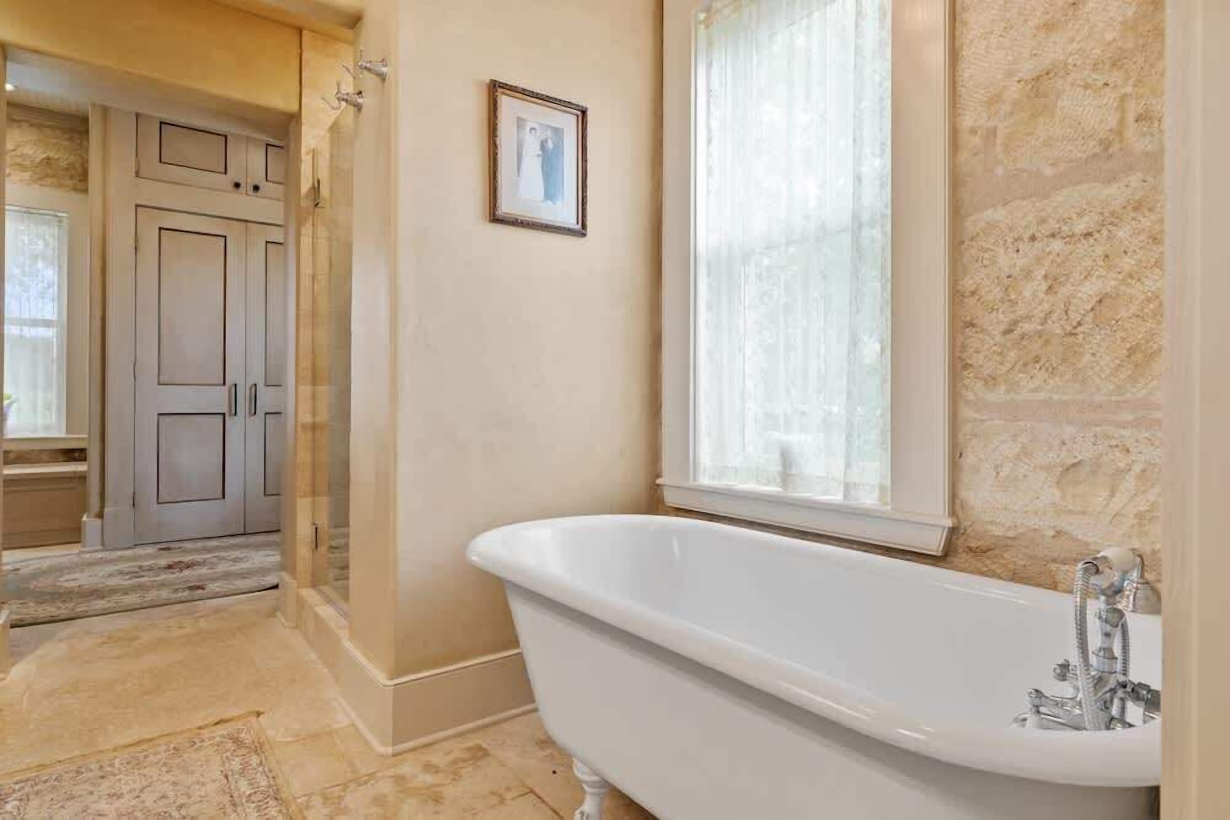 A bathroom with a freestanding bathtub, a shower, and a window with curtains.