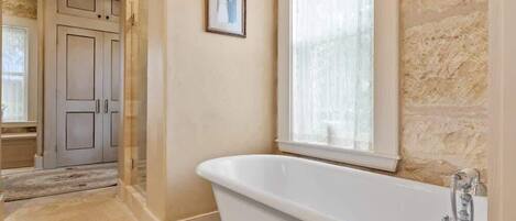 A bathroom with a freestanding bathtub, a shower, and a window with curtains.