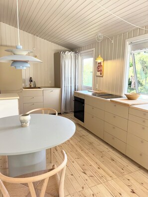 Uma cozinha moderna com uma mesa de jantar redonda, piso de madeira e uma janela com vista para o verde.