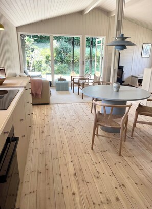 A spacious room with a large dining table, wooden flooring, and a view of greenery through large windows. - Classic Danish summer house (Asnæs)