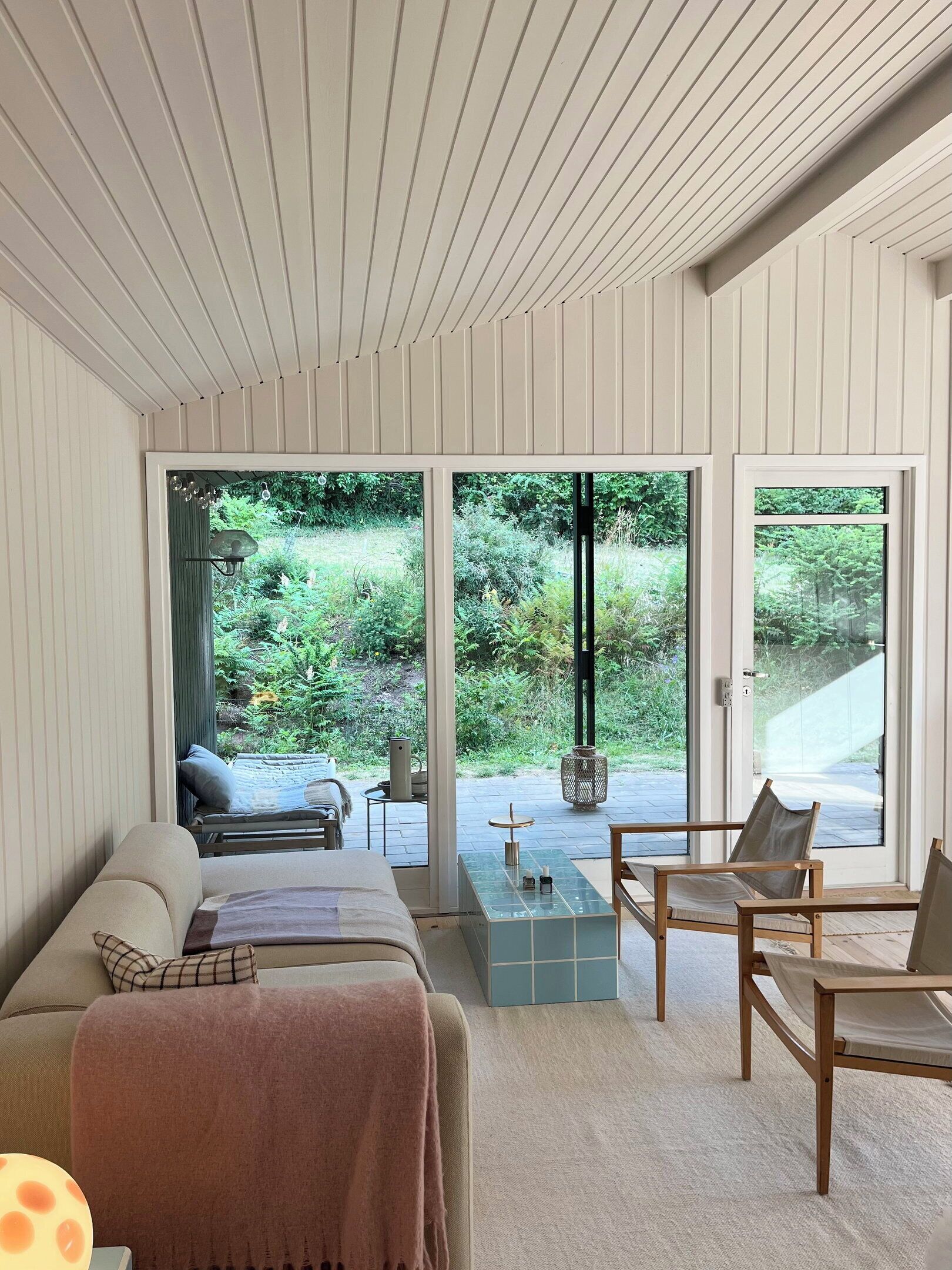 A modern interior with a bed, seating area, and large glass doors leading to a garden.