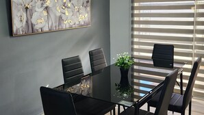 A dining area with a black table and chairs, a potted plant, and a large floral painting on the wall.
