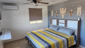 Un dormitorio con cama, ventilador de techo, ventana con persianas y adornos en la pared.