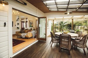 Ein offener Wohnbereich mit einer Couch, einem Esstisch mit Stühlen und einer Glasdoor, die zu einem Garten führt.