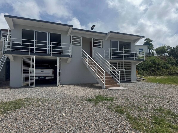 A two-story building with a car parked in the driveway, a staircase leading to the upper level, and a clear sky. - Rico Puerto Magic Spot Oeste (Cabrera)