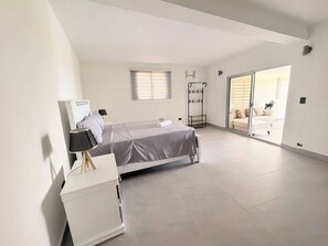 A modern bedroom with a bed, a desk, and a chair. There is a window with blinds, a radiator, and a sliding glass door leading to another room. - Rico Puerto Magic Spot Oeste (Cabrera)