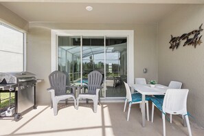 An outdoor patio with a grill, chairs, a table, and a glass door leading to a covered area. - ViLla dReaMs PoOl +Game Room NeAr DiSnEy (Kissimmee)