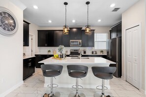 A modern kitchen with a central island, black cabinets, stainless steel appliances, and pendant lighting. - ViLla dReaMs PoOl +Game Room NeAr DiSnEy (Kissimmee)