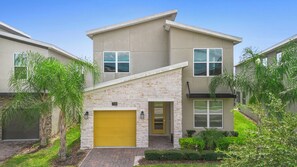 A modern two-story residential building with a stone facade, a yellow garage door, and a well-maintained front yard with greenery. - ViLla dReaMs PoOl +Game Room NeAr DiSnEy (Kissimmee)