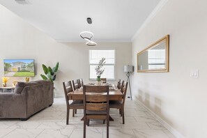 A dining area with a wooden table, chairs, and a vase with flowers. There is a couch and a floor lamp in the room. - ViLla dReaMs PoOl +Game Room NeAr DiSnEy (Kissimmee)