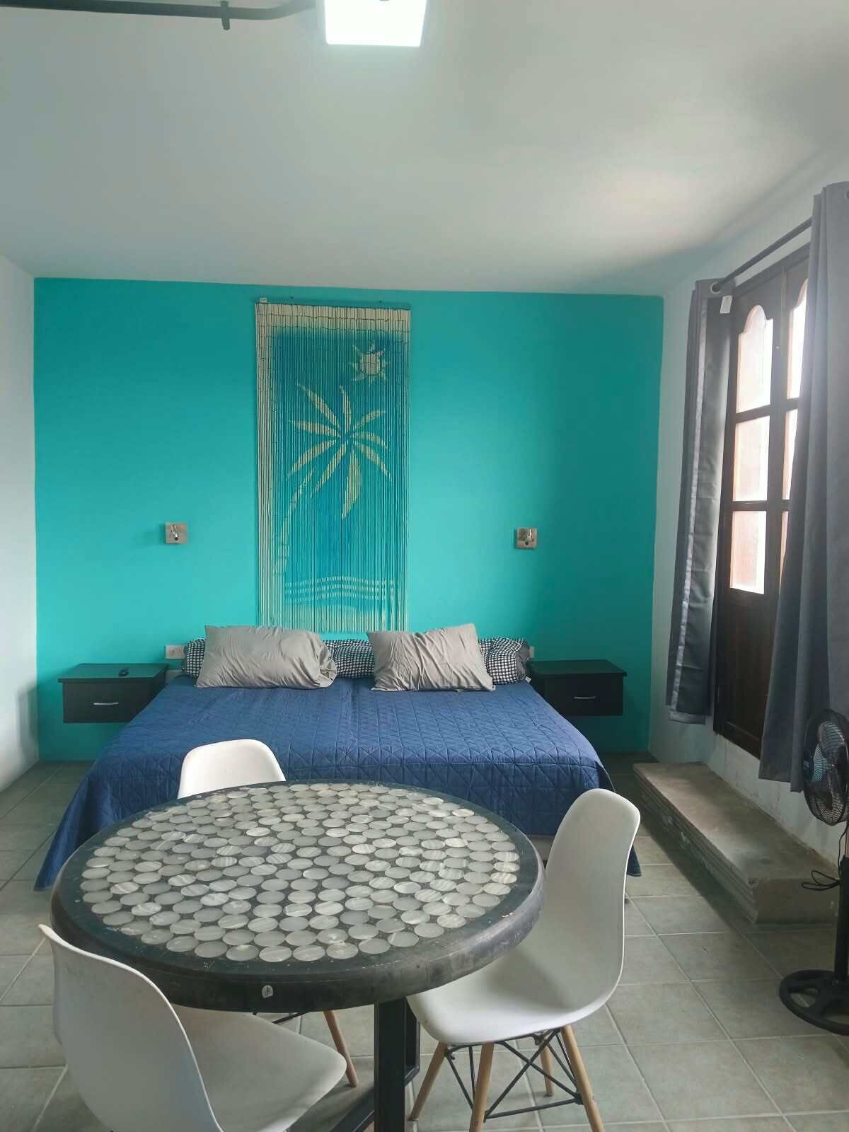 A room with a bed, a table with chairs, a window, and a curtain.