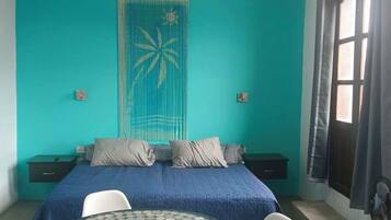 A room with a bed, a table with chairs, a window, and a curtain.