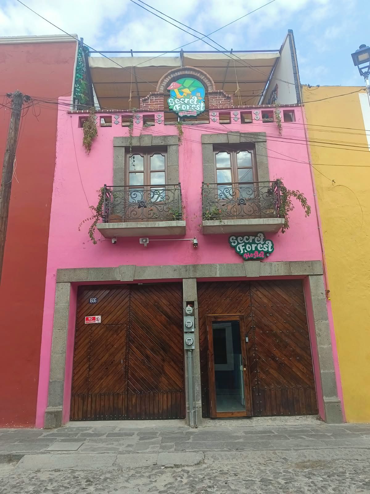 Un edificio rosa con un letrero que dice 'Secret Forest Hostel' y una puerta de madera grande.