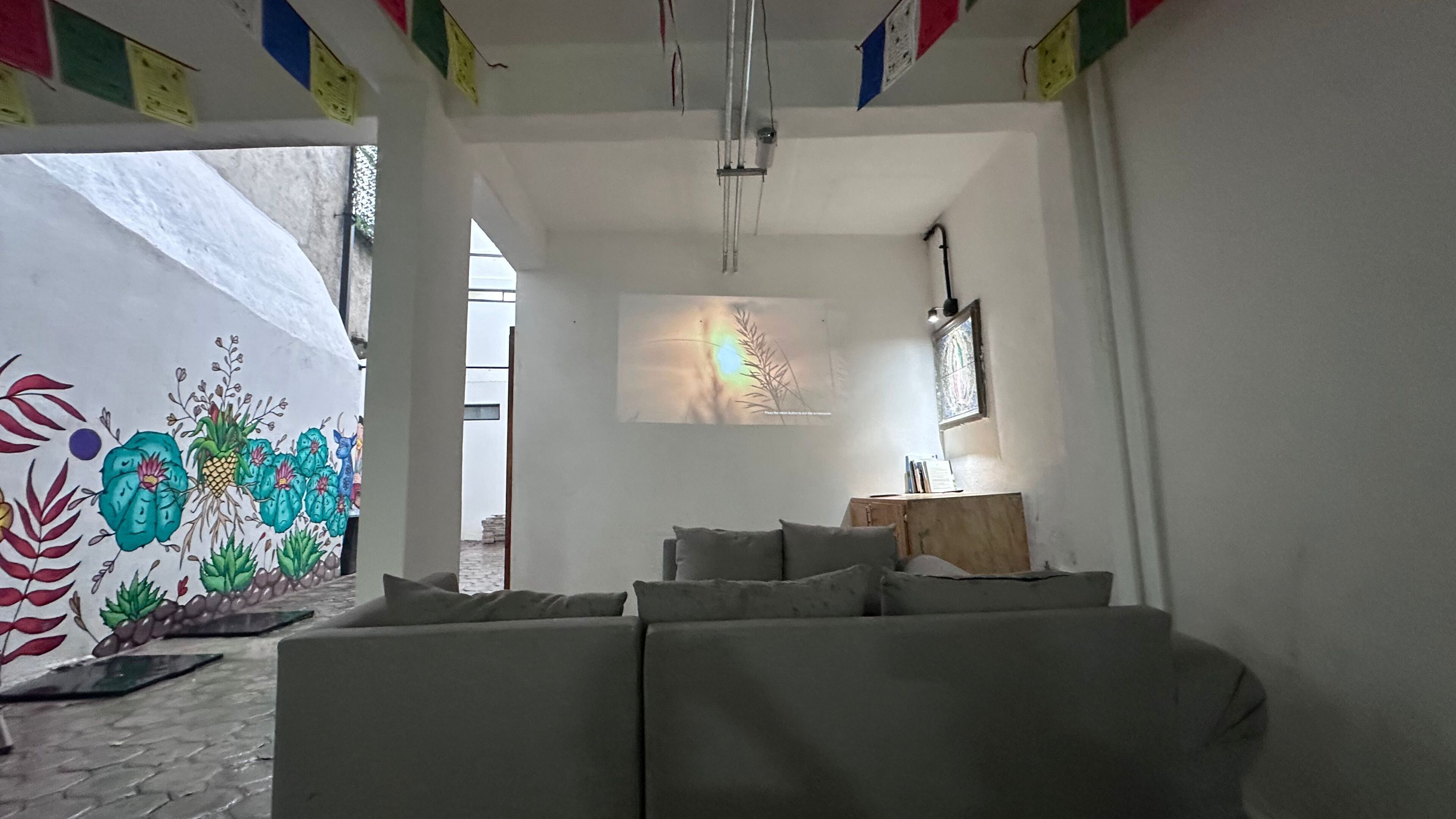 Ett rum med en soffa, en projektorduk och en vägg prydd med en färgstark väggmålning.
