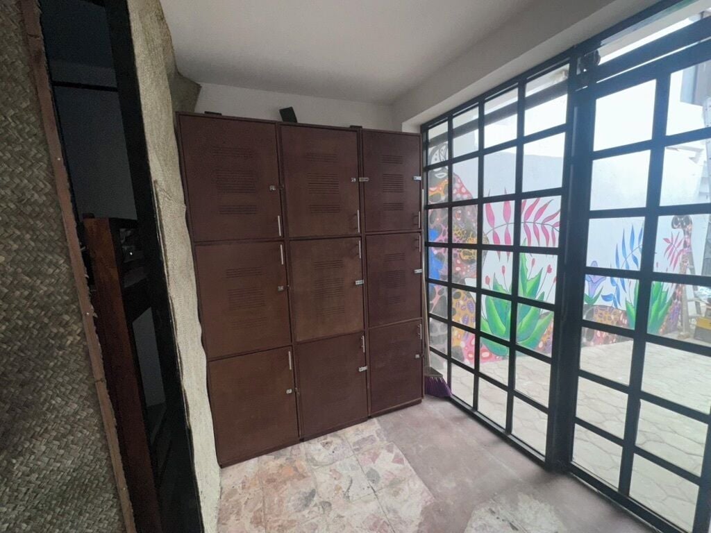 Una habitación con un amplio ventanal corredero que da a un espacio exterior, un armario metálico marrón y suelo de baldosas.