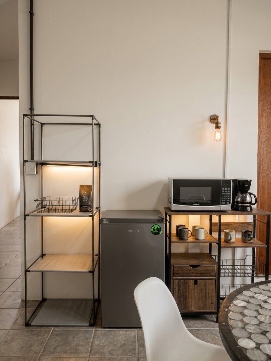 Uma cozinha compacta equipada com micro-ondas, máquina de café e estantes para armazenamento.
