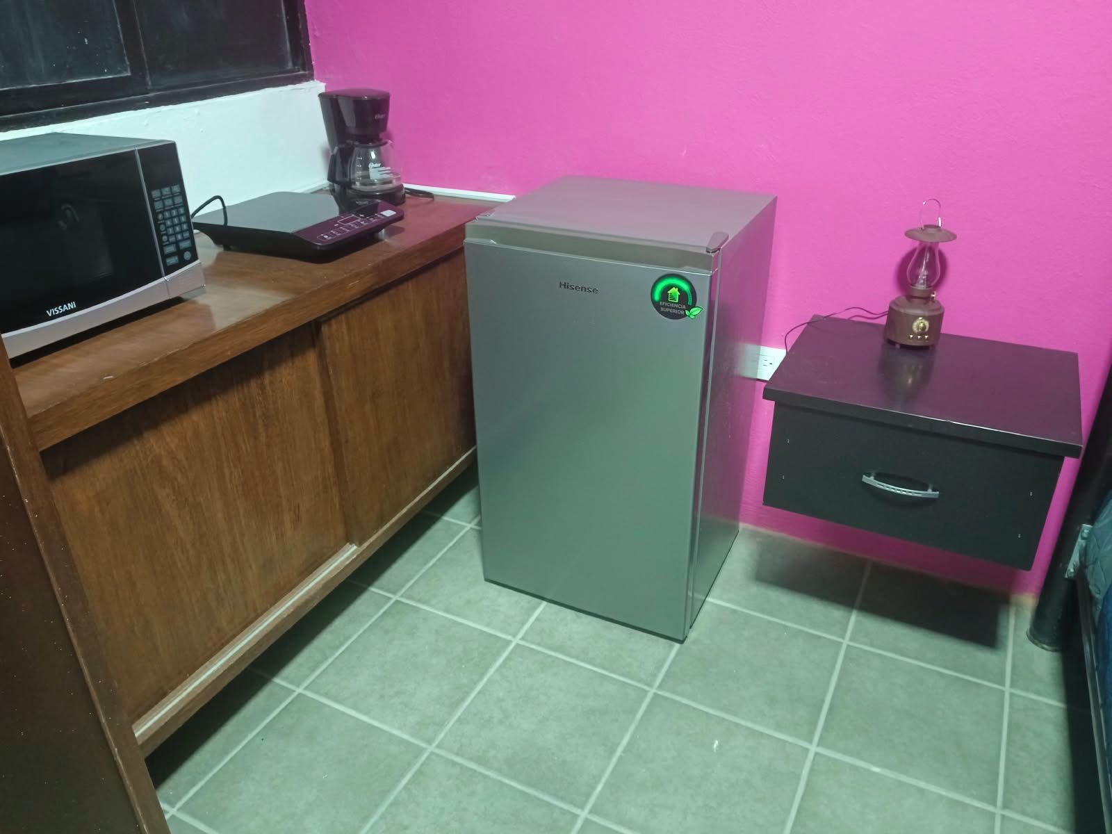 Una cocina compacta con microondas, cafetera, refrigerador y un mueble pequeño.