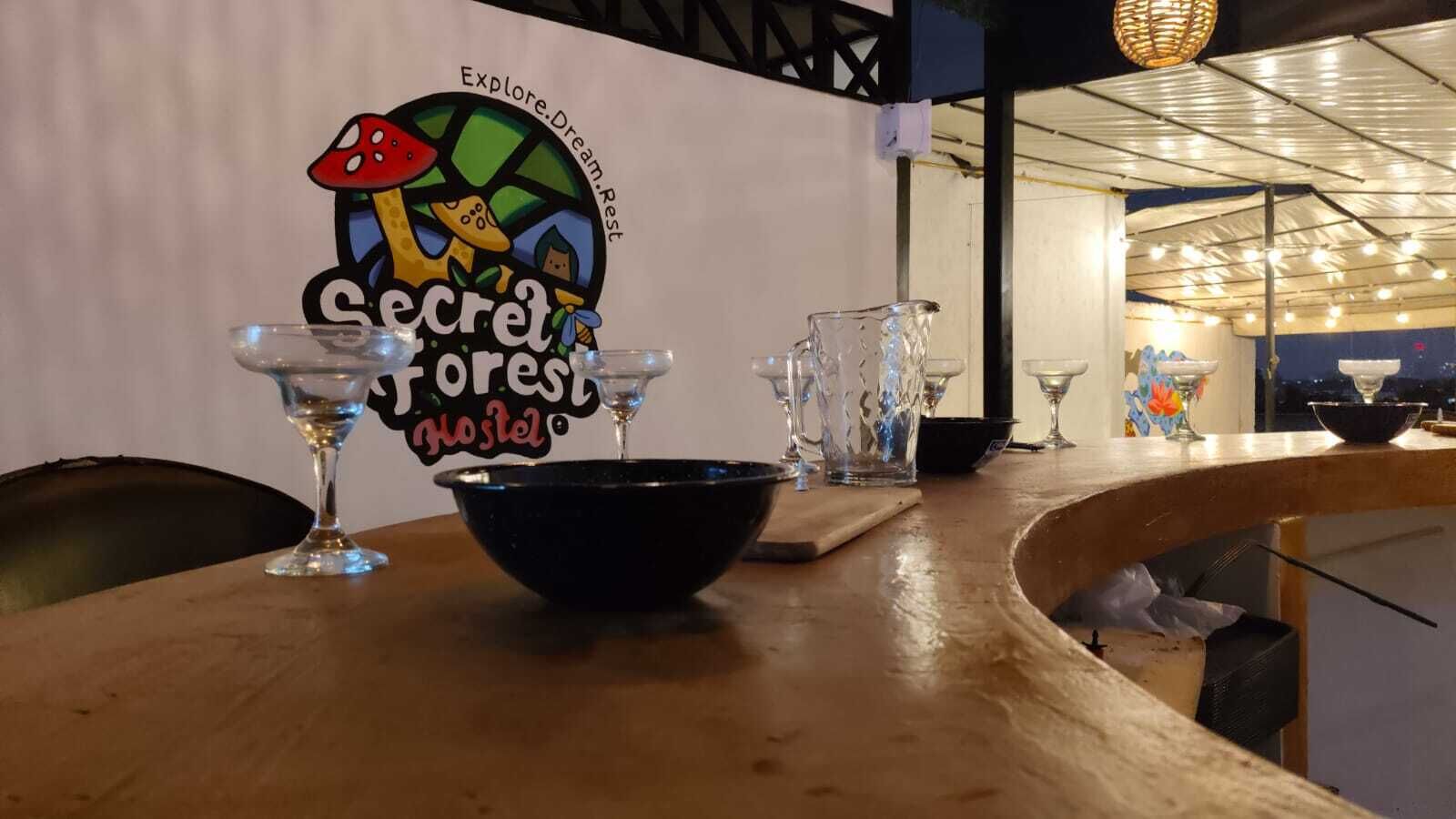 Una mesa con un tazón, un vaso y un cartel para 'Secret Forest Hostel' con un diseño de hongos y bosque.