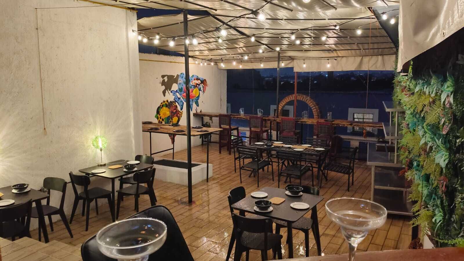 An indoor dining area with multiple tables and chairs, a mural on the wall, and a tent-like structure overhead.