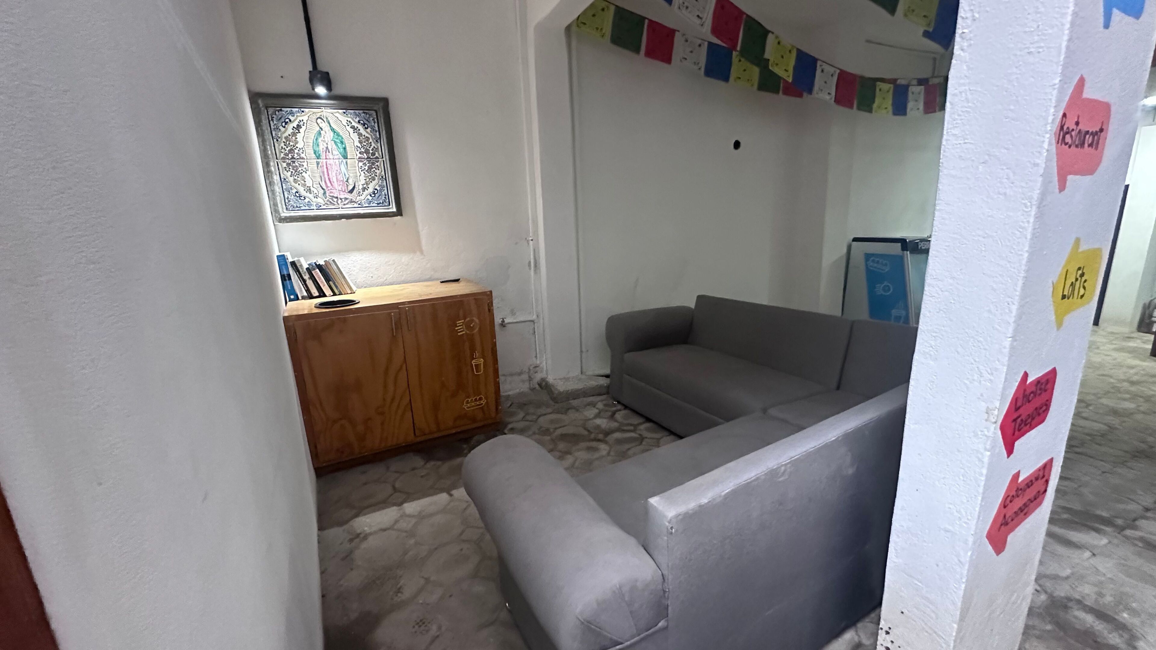A room with a grey sofa, a wooden cabinet, and a wall-mounted picture. There are signs indicating a restaurant and lofts.